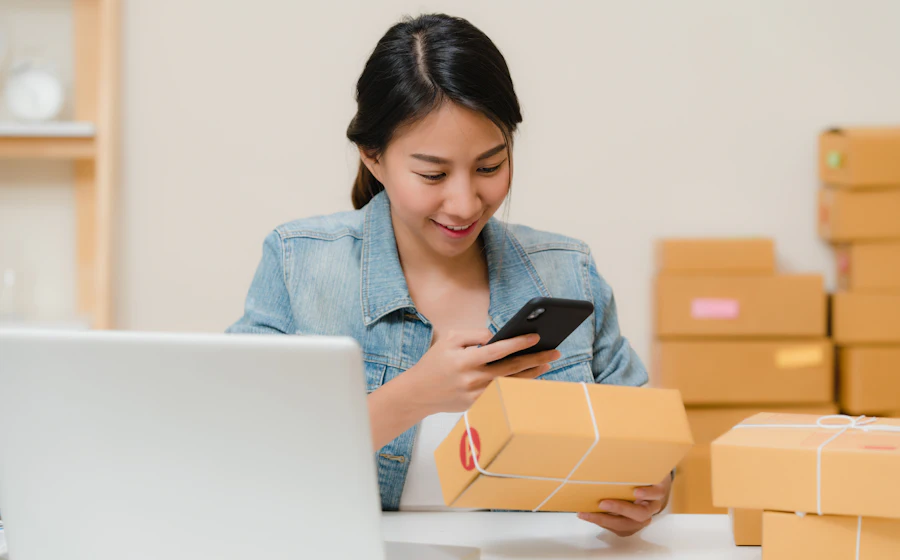 Small business owner checking an order on her phone next to packed boxes
